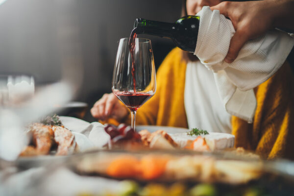 Romantic young caucasian man pouring red wine for his girlfriend during dinner date at restaurant enjoying healthy food, romantic atmosphere, happy couple celebrating concept