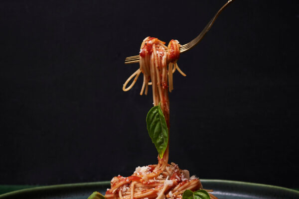 spaghetti with tomato sauce and basil leaves om dark green plate